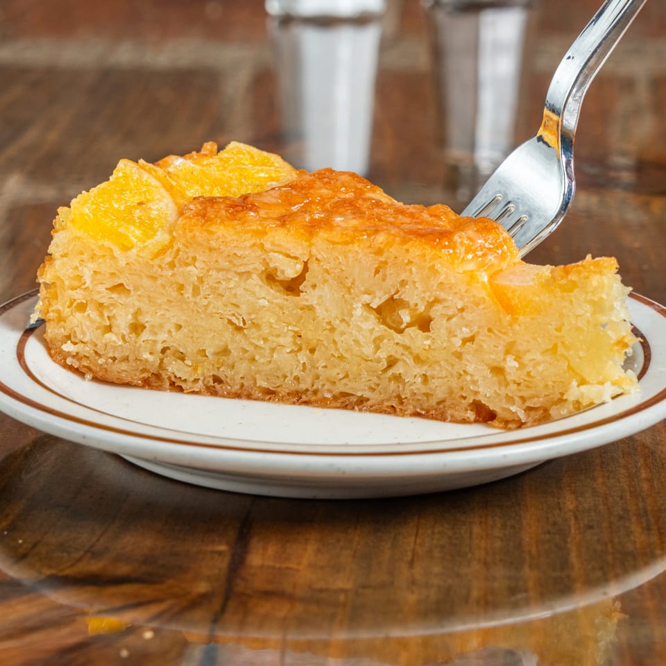 A fork is taking a bite from a slice of golden-brown pineapple upside-down cake on a white plate.