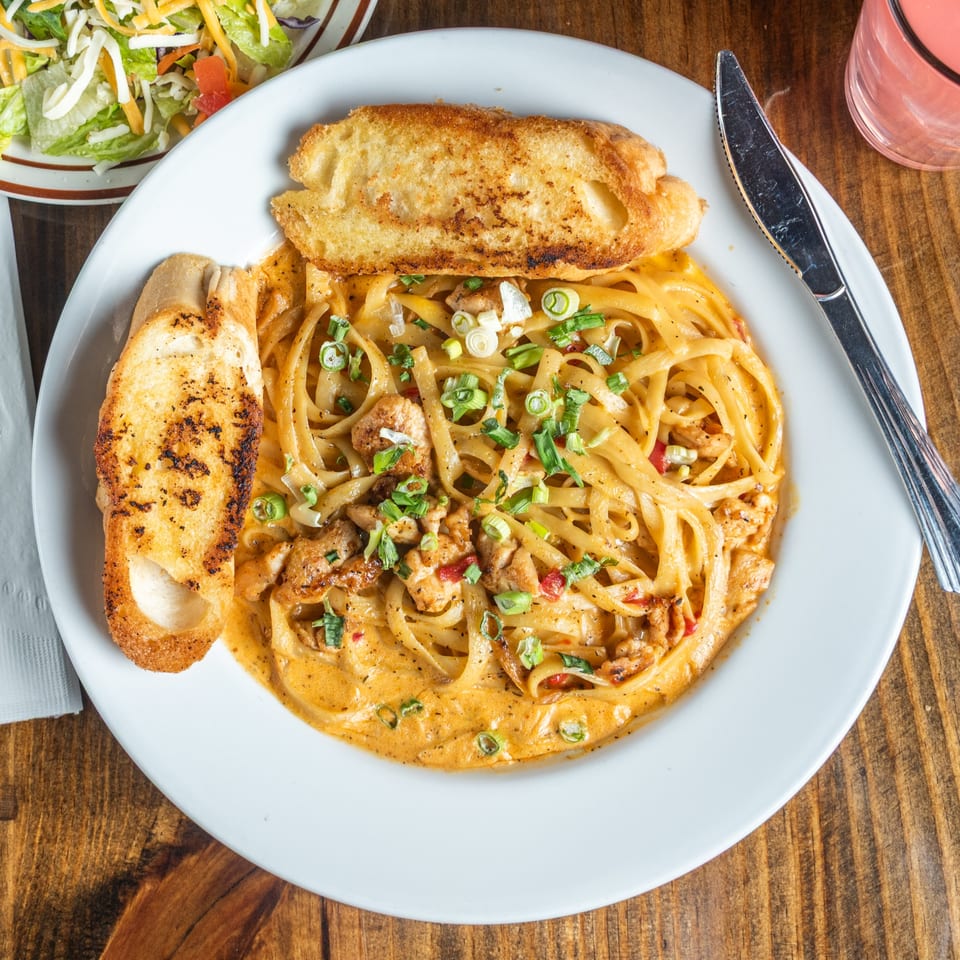Good Times Grill's creamy chicken pasta with garlic bread, a side salad, and a pink drink.