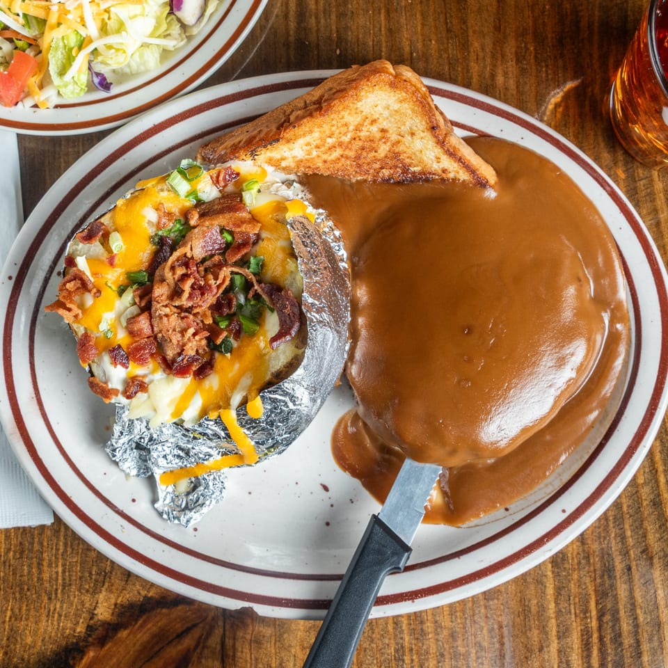 Good Times Grill's loaded baked potato with cheese, bacon, and green onions, alongside a steak smothered in gravy.